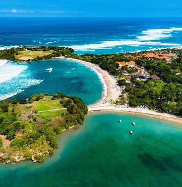 Aerial view of the stunning Nusa Dua coastline in Bali, featuring twin turquoise bays, white sand beaches, lush green headlands, and resort developments.